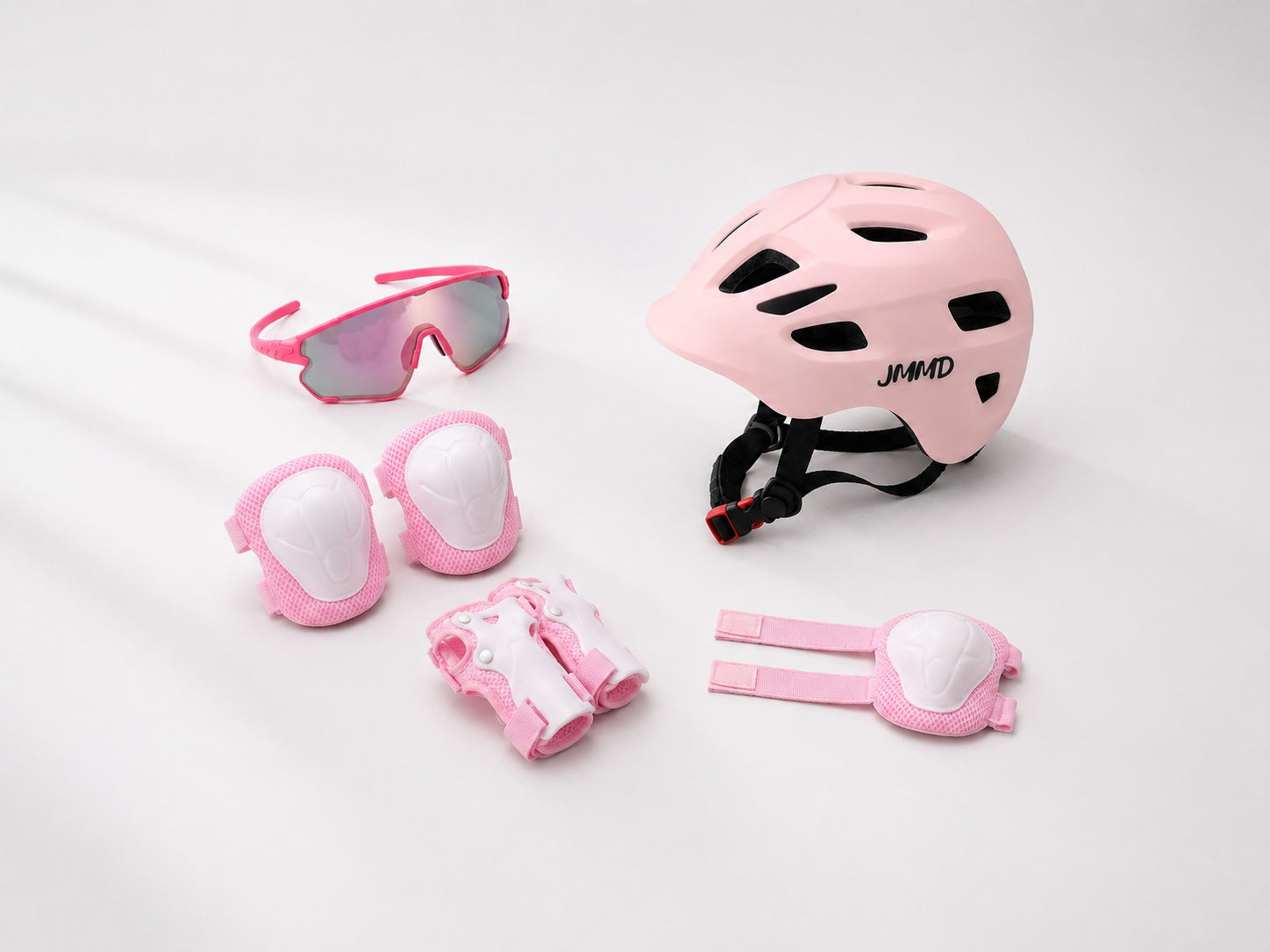 Pink JMMD kids bike helmet and protective pads set with sports glasses on a white studio background