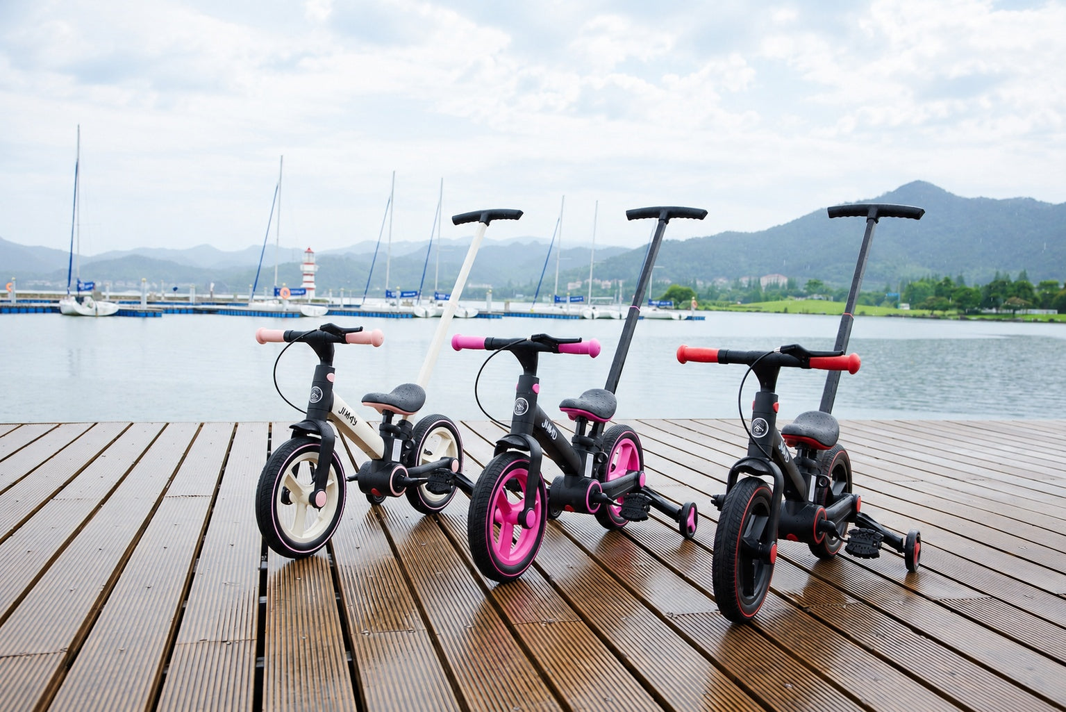 Three JMMD kids trikes with push handles displayed on a lakeside wooden deck